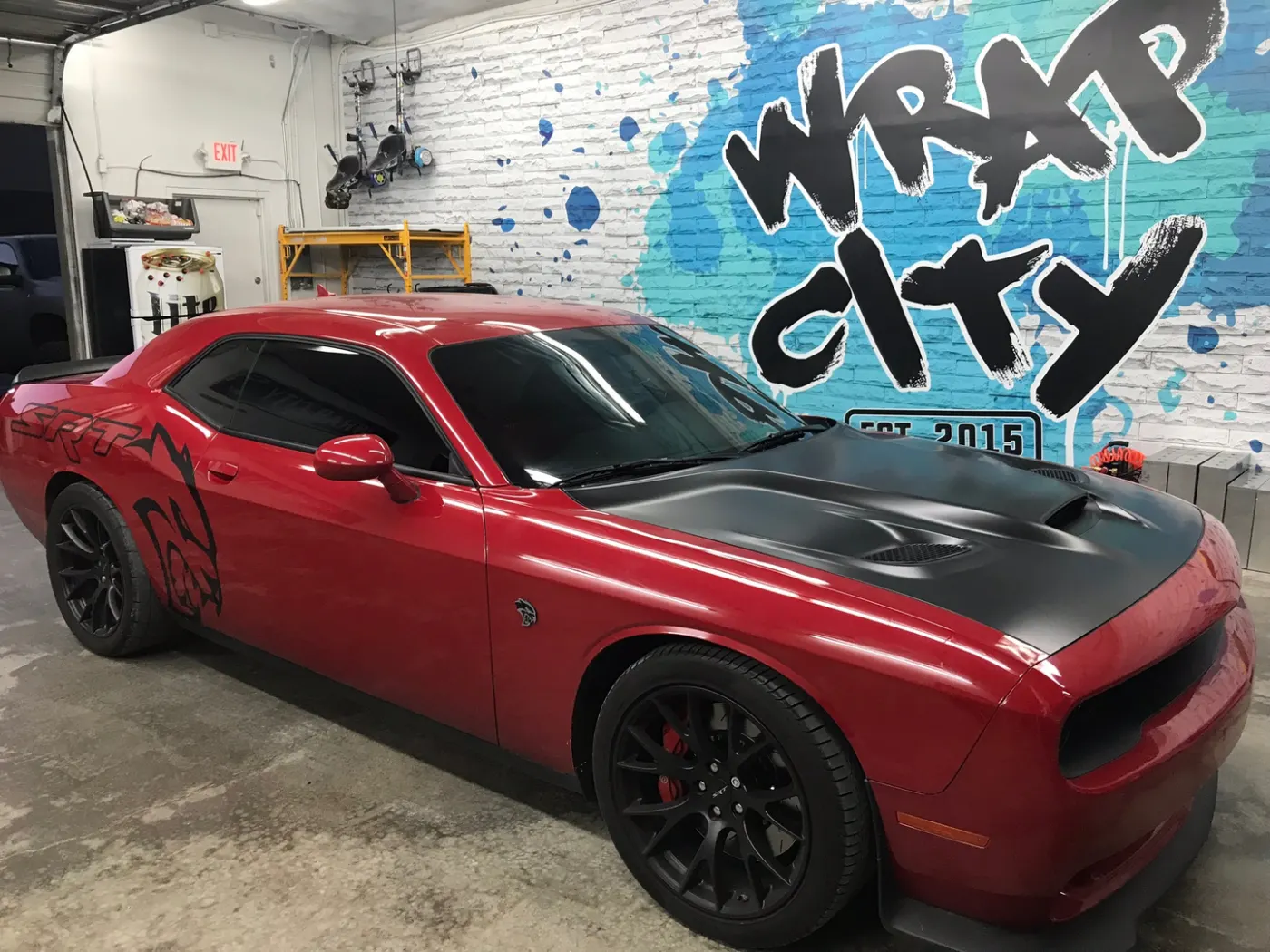 Muscle car with a gloss black hood and roof laid over the factory red — a two-panel change, not a full wrap.