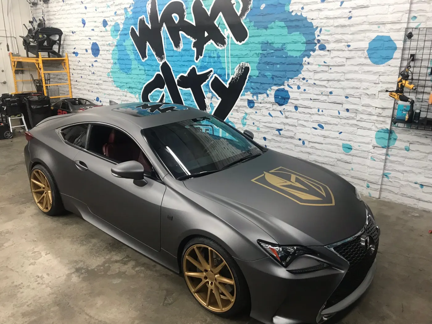 Matte grey coupe with a cut gold shield on the door and gold wheels to match.