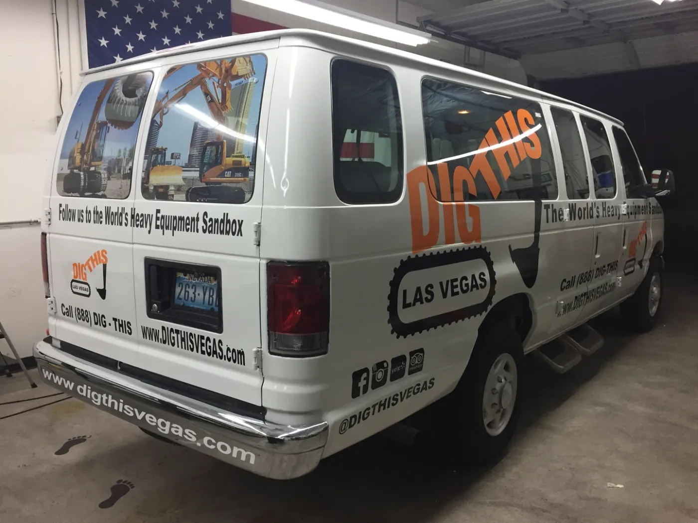 Full-size passenger van printed with heavy-equipment photography and social handles down the rear quarter.
