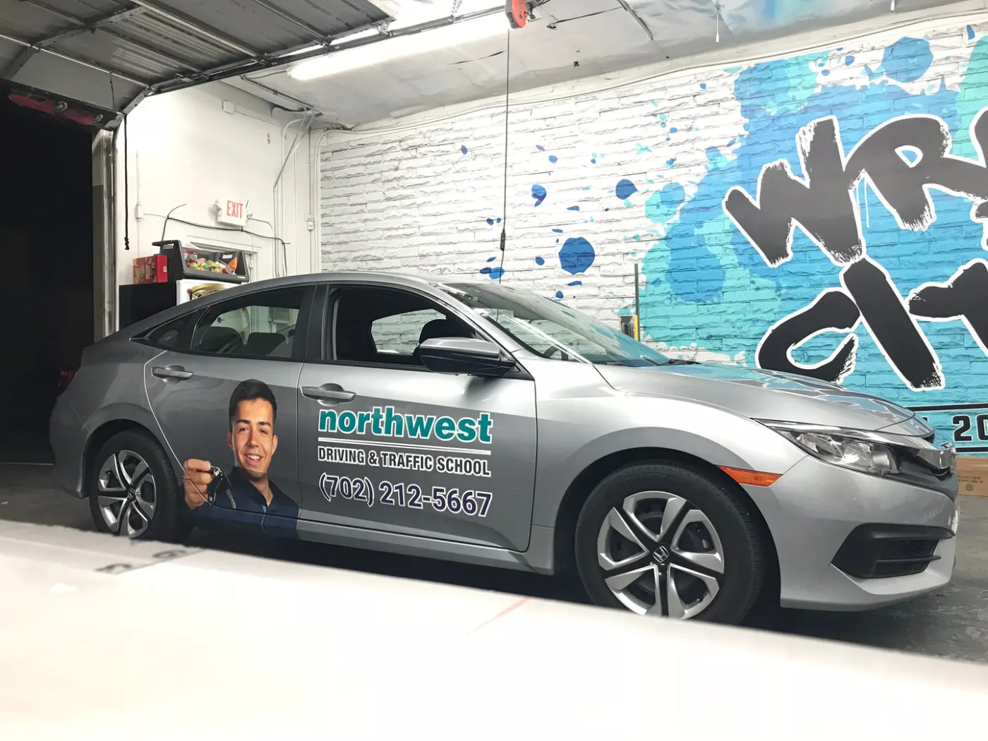 Sedan in a partial wrap: printed panel graphics and a phone number over the factory silver.