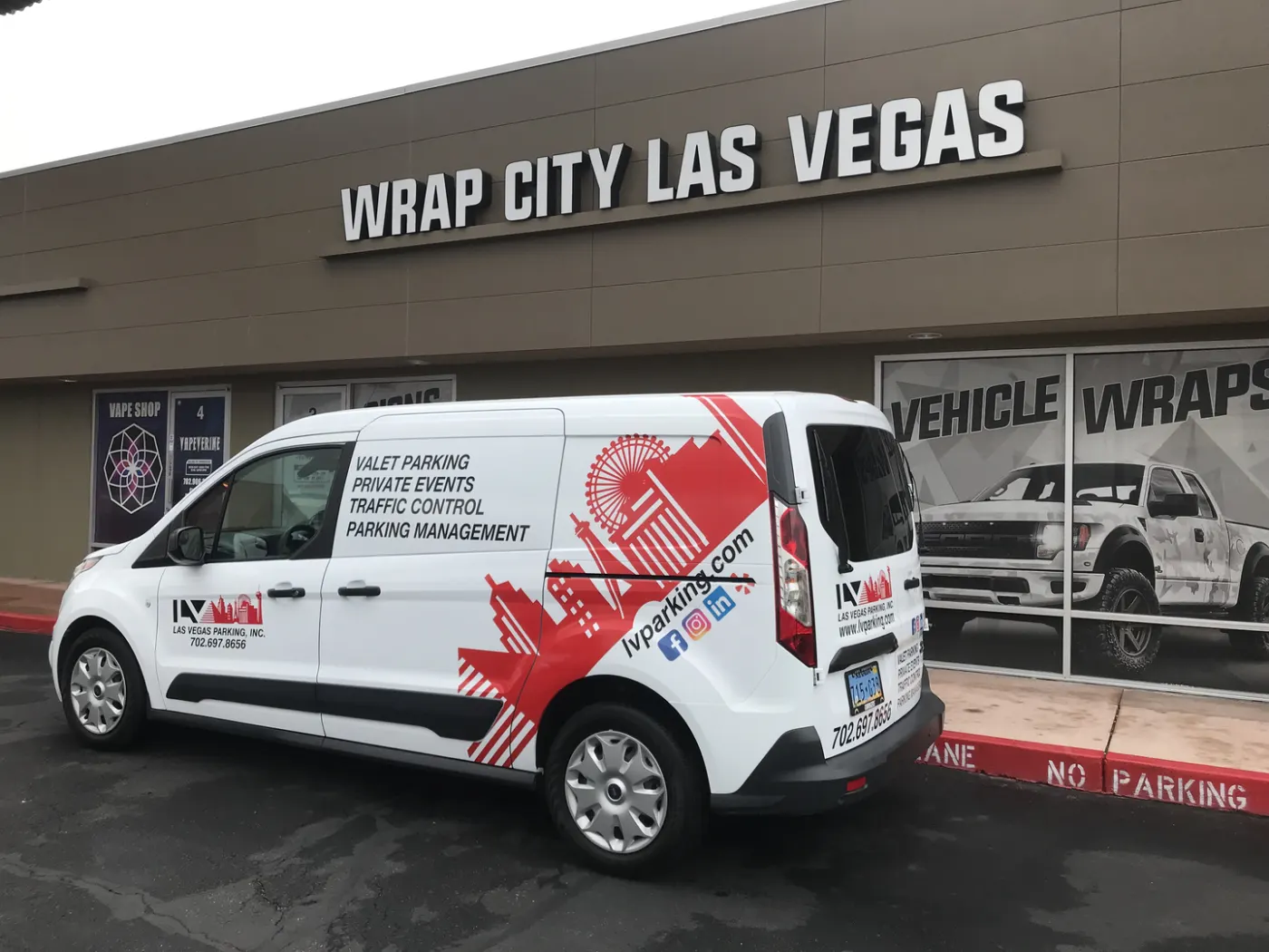 Compact cargo van in a red-and-white geometric print wrap, parked in front of the shop.