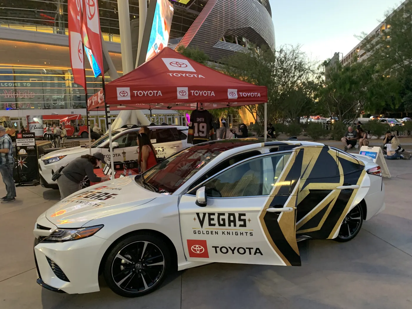 The team-wrapped sedan on display at an outdoor event, doors open under the tents.